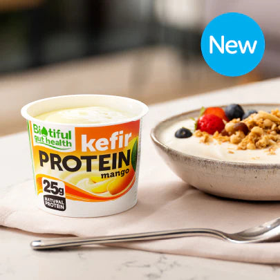 Image of kefir protein mango yogurt pot on a table next to a spoon and serving suggestion of yogurt and fruit